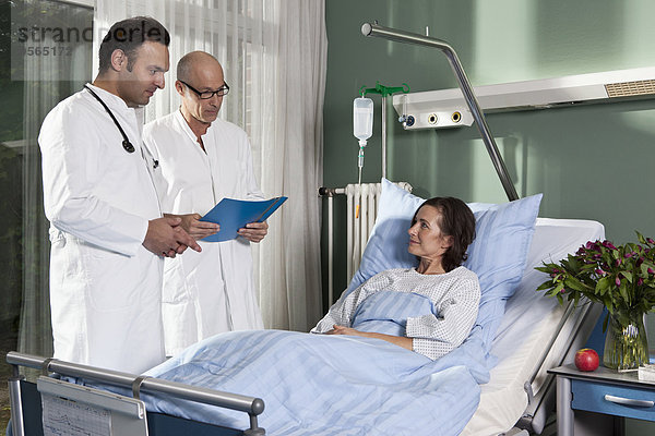 Zwei Ärzte neben einer Patientin auf einer Krankenstation