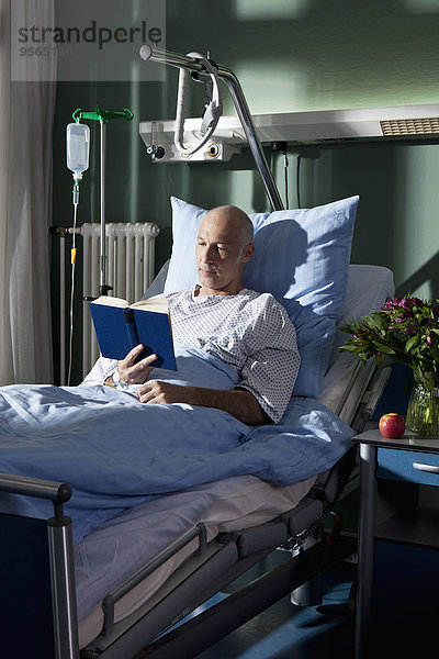 Ein Mann  der ein Buch in einem Krankenhausbett liest.
