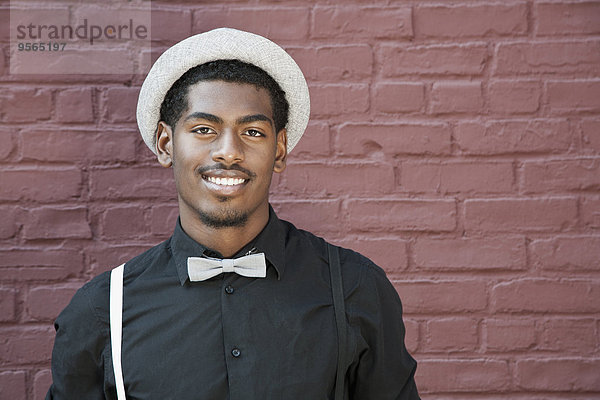 Ein fröhlicher junger schwarzer Mann mit Fliege  Hosenträgern und Hut.