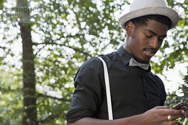 Ein schwarzer Mann mit Fliege und Hosenträgern  der ein Handy benutzt.