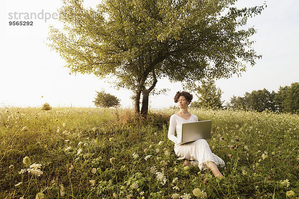 Frau mit Laptop entspannt auf dem Feld