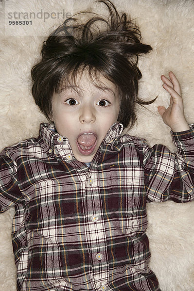 Porträt eines geschockten Jungen mit offenem Mund auf einem Teppich liegend