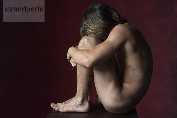 Nackter Mann sitzend in fetaler Position  Seitenansicht