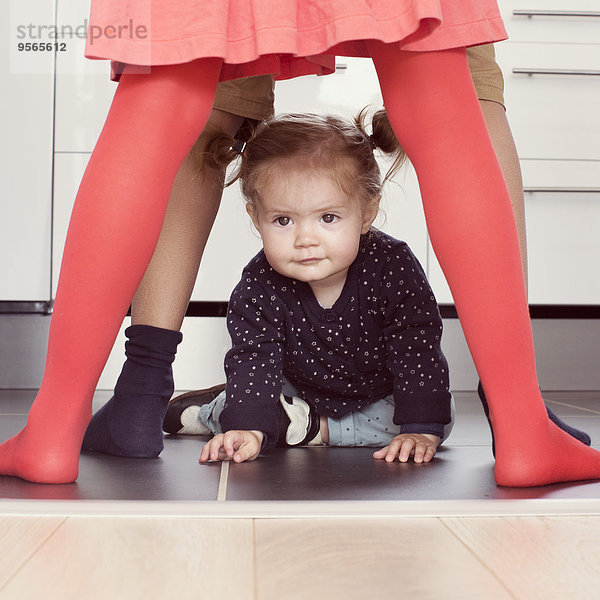 Kleines Mädchen krabbelt durch die Beine von Geschwistern