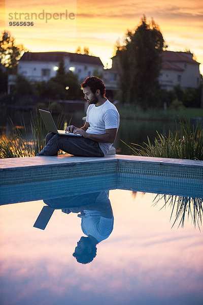 Mann mit Laptop neben dem Schwimmbad als Sonnenuntergang