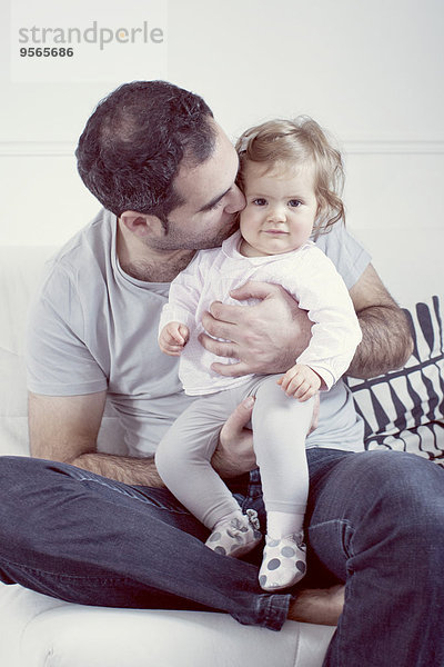 Vater hält das Mädchen auf dem Schoß und küsst seine Wange.