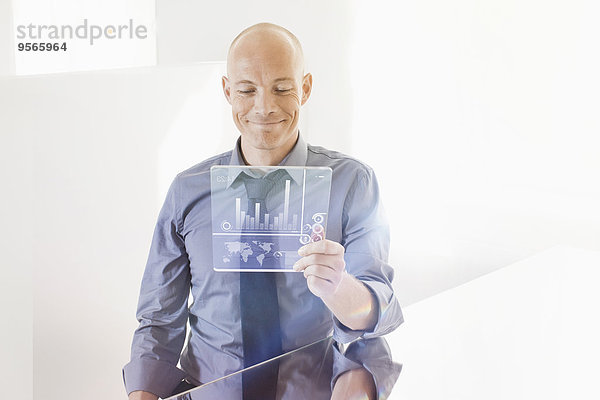 Lächelnder Geschäftsmann betrachtet futuristisches digitales Tablett am Schreibtisch im Büro