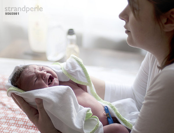 Frau hält weinendes Neugeborenes in der Hand
