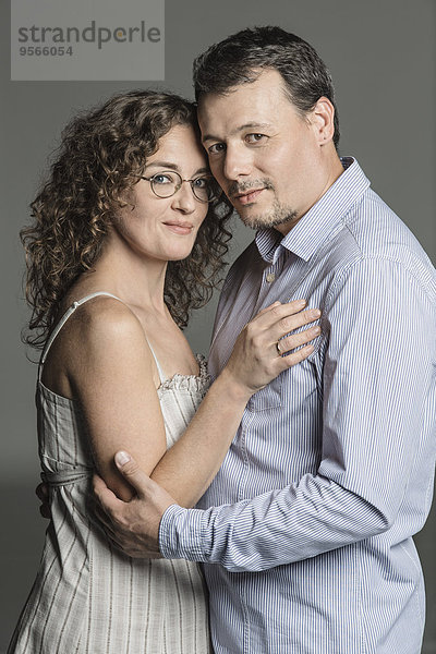 Seitenansicht Porträt eines liebenden Paares  das sich vor grauem Hintergrund umarmt.