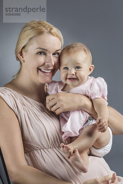 Porträt der glücklichen Mutter mit süßem Mädchen vor grauem Hintergrund