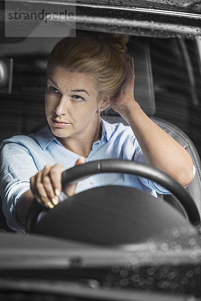 Mittlere erwachsene Frau  die sich selbst im Rückspiegel beim Autofahren ansieht