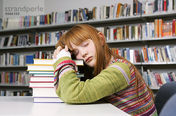 Ein Mädchen macht ein Nickerchen auf einem Stapel Bücher in einer Bibliothek.