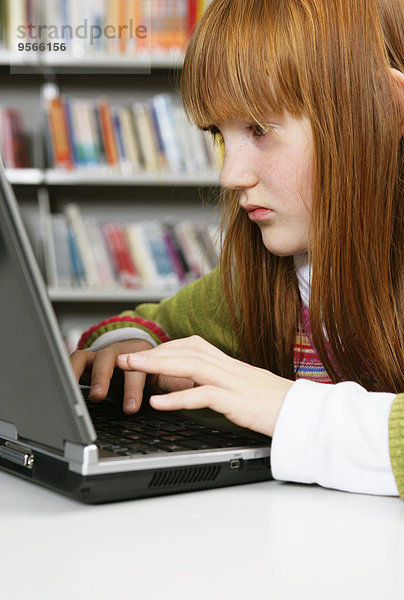 Ein Mädchen arbeitet an einem Laptop in einer Bibliothek.