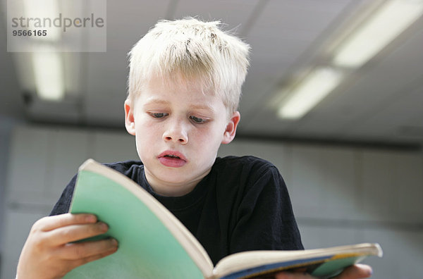 Vorderansicht eines kleinen Jungen beim aufmerksamen Lesen eines Buches