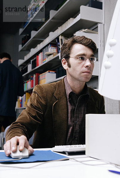 Ein Mann  der an einem Computer in einer Bibliothek arbeitet.