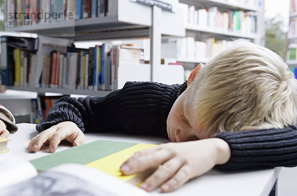 Ein Junge macht ein Nickerchen auf einem Schreibtisch in einer Bibliothek.