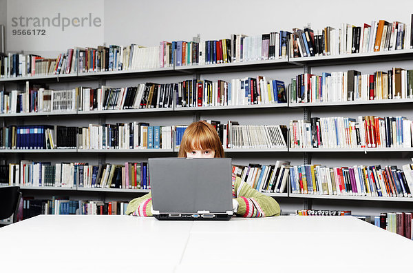 Ein Mädchen  das an einem Laptop in einer Bibliothek arbeitet.