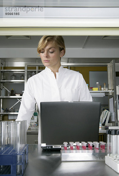 Eine Frau in einem Laborkittel in der Nähe eines Laptops.