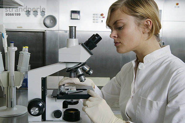 Eine Frau  die durch ein Mikroskop schaut.