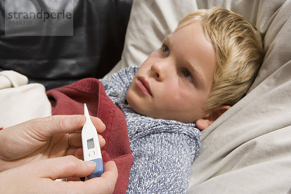 Krankes Kind auf dem Rücken liegend mit digitalem Thermometer