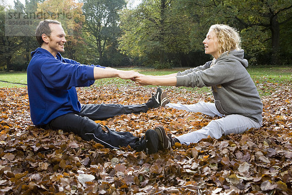 Mann und Frau sitzend und streckend auf Herbstlaub im Park