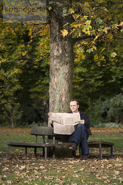 Ein reifer Mann sitzt auf einer Parkbank und liest eine Zeitung.
