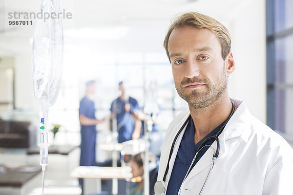 Porträt eines Arztes mittlerer Größe mit Kollegen im Hintergrund  stehend auf der Krankenstation