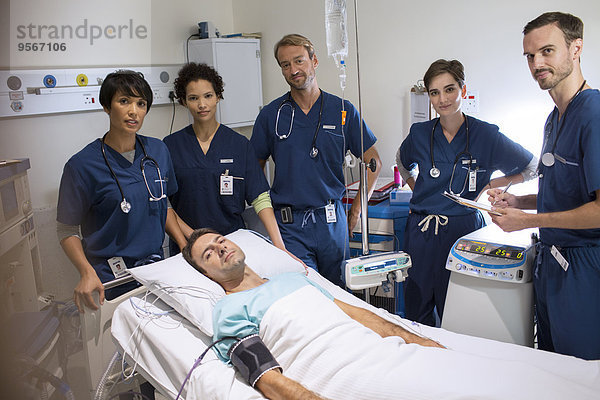 Ärzteteam um lächelnden Patienten im Bett auf der Intensivstation stehend