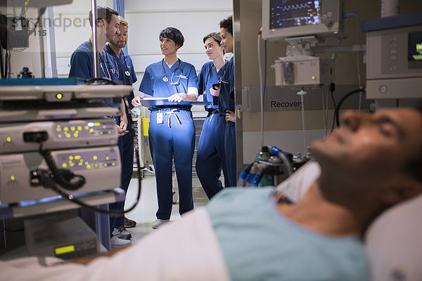 Patient an medizinische Überwachungsgeräte auf der Intensivstation angeschlossen  Ärzte im Eingangsbereich stehend