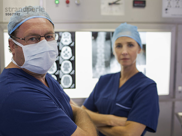 Portrait von Chirurgen mit gekreuzten Armen vor MRT-Scan und Röntgenbild
