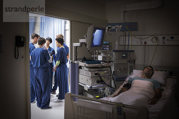 Patient liegt im Bett auf der Intensivstation  Ärzteteam diskutiert im Hintergrund