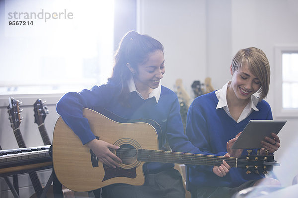 Studentinnen spielen Akustikgitarre im Klassenzimmer und benutzen den Tablet PC.