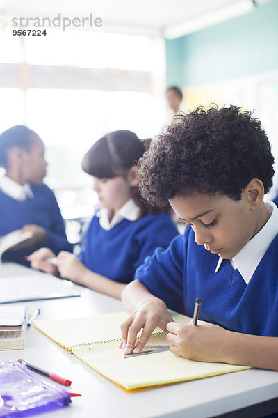 Schülerzeichnung im Notizbuch am Schreibtisch im Klassenzimmer  Mädchen im Hintergrund
