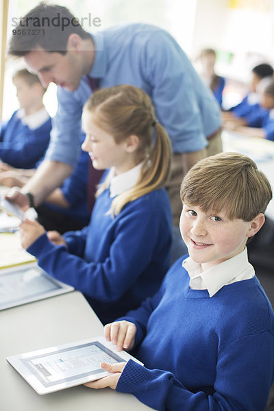 Porträt eines Schülers mit digitalem Tablett im Klassenzimmer  Kinder und Lehrer im Hintergrund