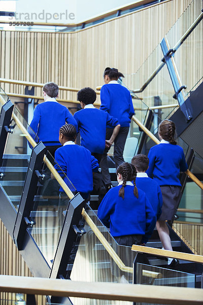 Rückansicht einer Gruppe von Schülern in blauen Schuluniformen  die in der Schule die Treppe hinaufgehen.