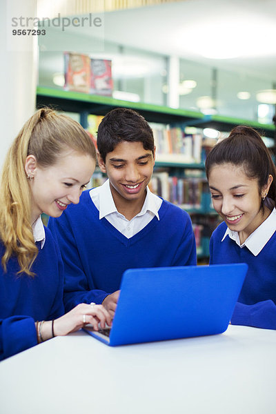 Drei fröhliche Studenten bei der Arbeit mit dem Laptop in der Bibliothek