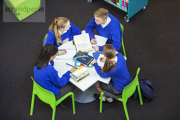 Overhead-Ansicht von vier Schülern bei ihren Hausaufgaben am runden Tisch