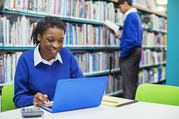 Lächelnde Studentin mit Laptop in der Bibliothek