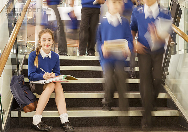 Porträt eines lächelnden Grundschulmädchens  das auf Stufen in der Schule sitzt