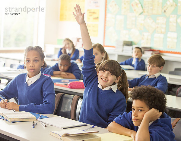 Grundschulkinder im Klassenzimmer während des Unterrichts  lächelndes Mädchen mit erhobener Hand