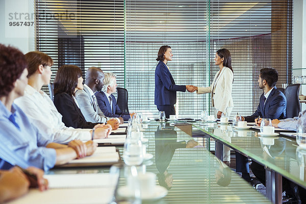 Zwei Geschäftsfrauen beim Händeschütteln im Konferenzraum  Kollegen beim Zuschauen