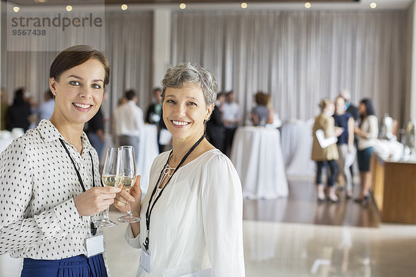 Zwei Geschäftsfrauen stehen mit Champagnerflöten in den Händen  Kollegen im Hintergrund