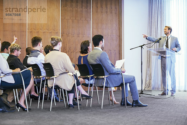 Porträt eines Geschäftsmannes am transparenten Rednerpult vor Publikum im Konferenzraum