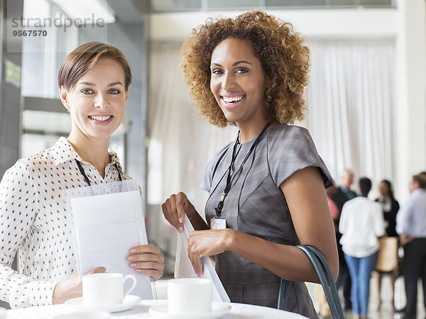 Porträt von zwei lächelnden Frauen  die während der Kaffeepause im Foyer des Konferenzzentrums stehen.