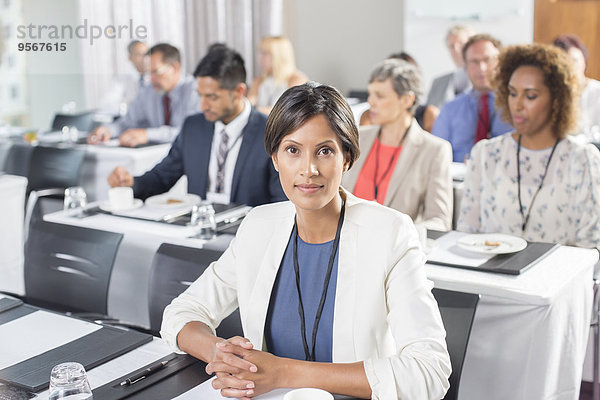 Porträt einer Frau mit einer Gruppe von Geschäftsleuten im Hintergrund beim Seminar