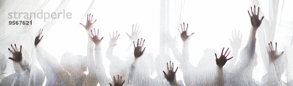 Silhouette von Menschen  die ihre Hände hinter einem transparenten Vorhang erheben.