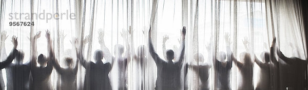 Silhouette von Menschen  die ihre Hände hinter einem transparenten Vorhang erheben.