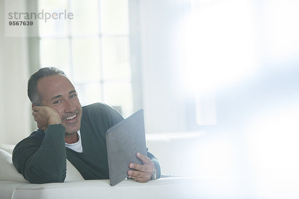 Älterer Mann mit digitalem Tablett auf dem Sofa