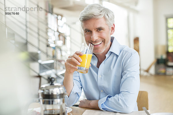 Älterer Mann trinkt Orangensaft am Frühstückstisch