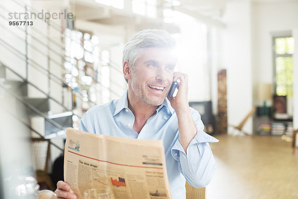 Älterer Mann im Gespräch am Handy mit Zeitung